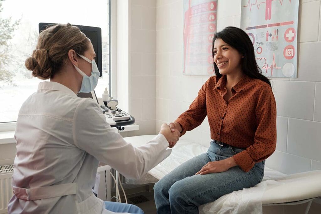 A clinician shakes hands with a smiling endocrinology patient in an ultrasound suite