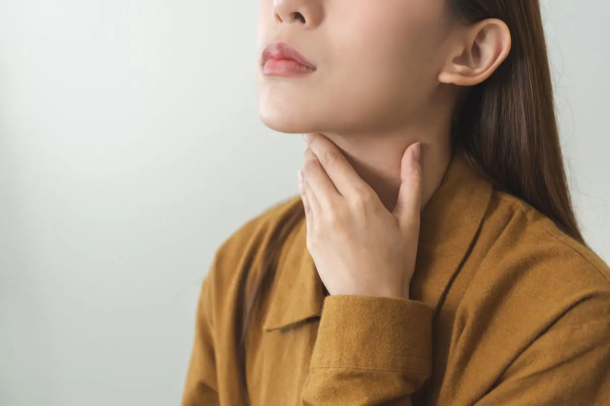 A young woman touches her neck over her thyroid