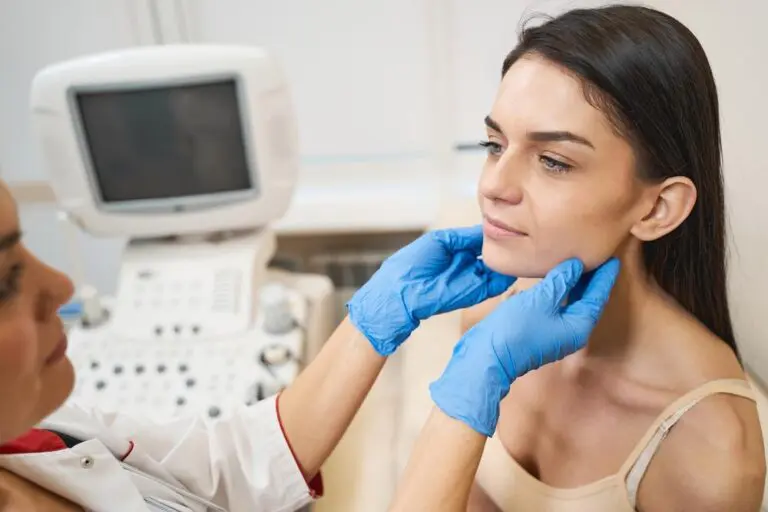 A patient receives a thyroid examination while seated beside an ultrasound machine.