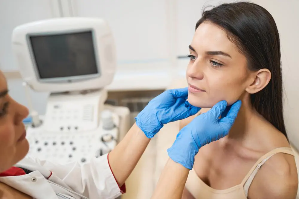 A patient receives a thyroid examination while seated beside an ultrasound machine.