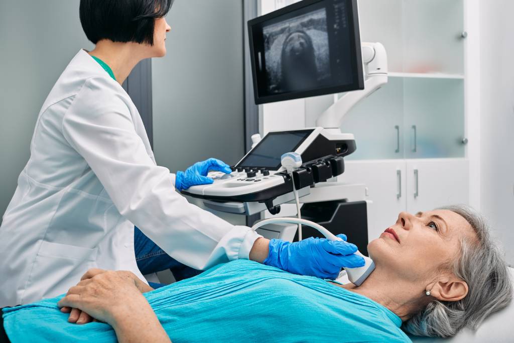 A clinician performs a thyroid ultrasound on an older female patient.