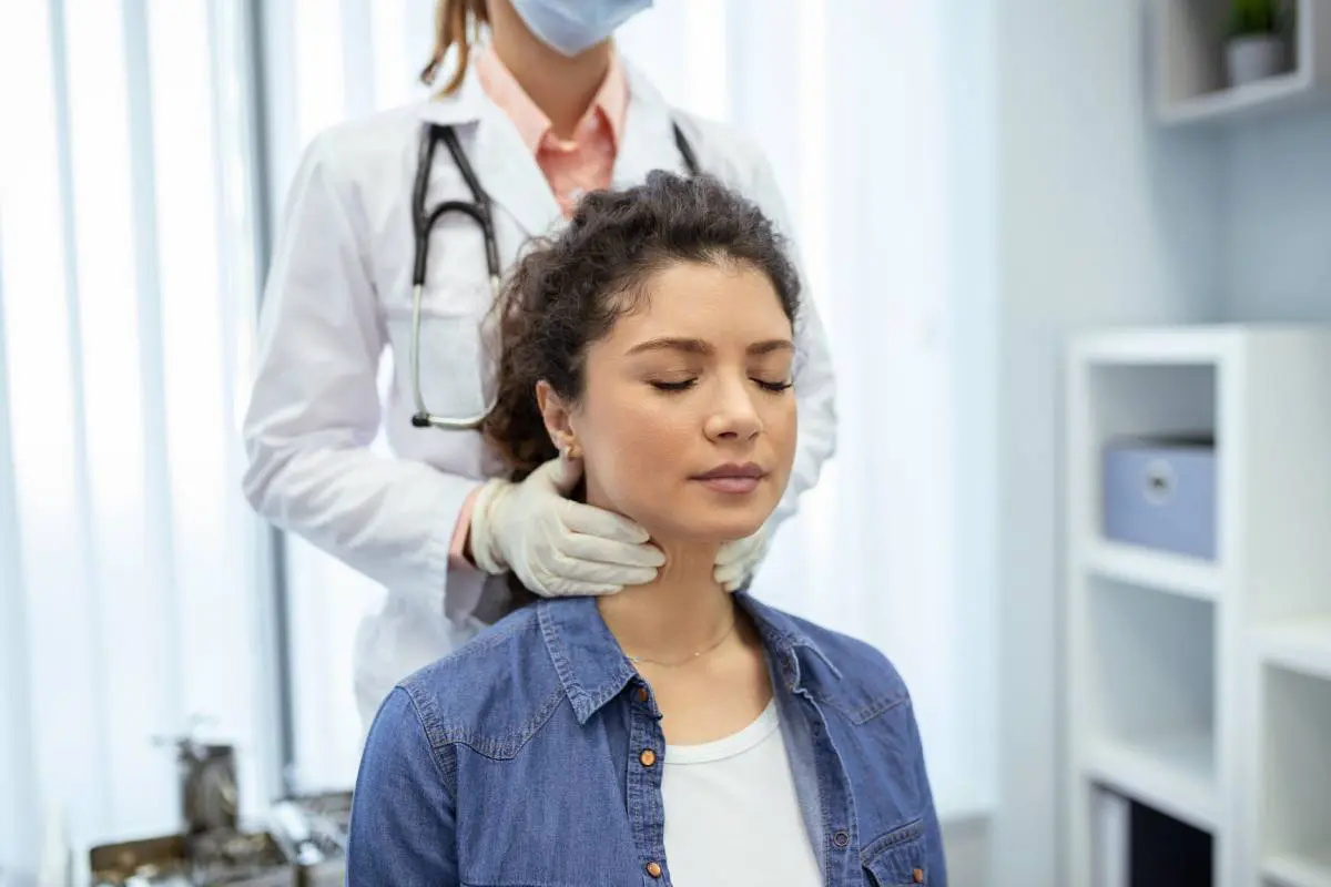 An endocrinologist examines the throat of a young woman in a medical office.
