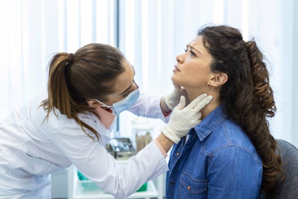 An endocrinologist examines the throat of a young woman in profile.