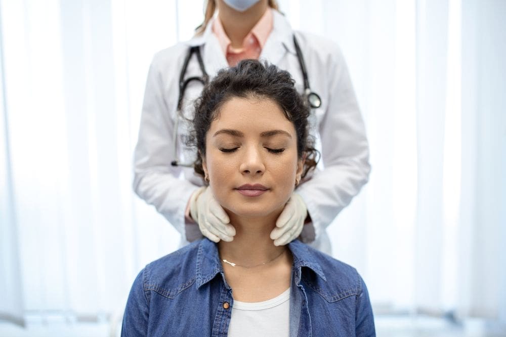 An endocrinologist palpates a woman's thyroid.