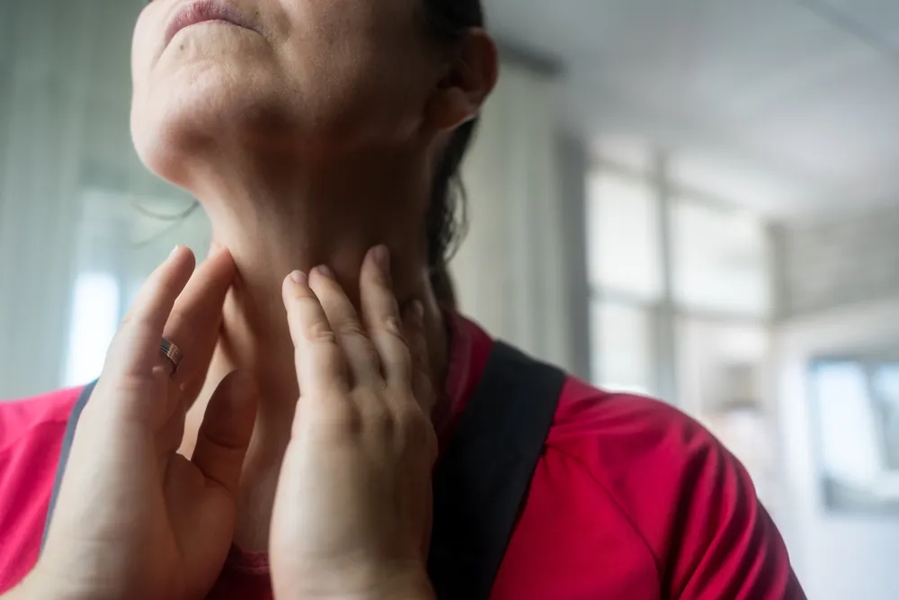 An older woman touches her thyroid with concern.
