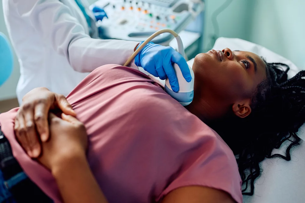 A clinician performs a thyroid ultrasound on a female patient.