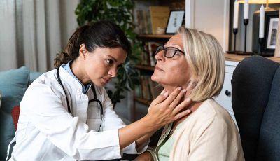 A clinician examines the thyroid of an older patient.