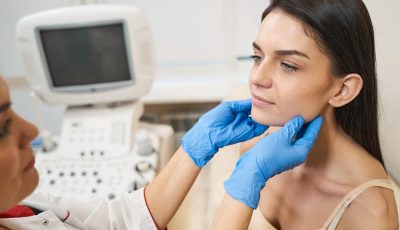 A patient receives a thyroid examination while seated beside an ultrasound machine.