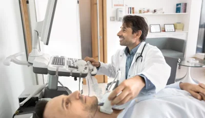 A grinning endocrinologist performs a thyroid ultrasound on a male patient.